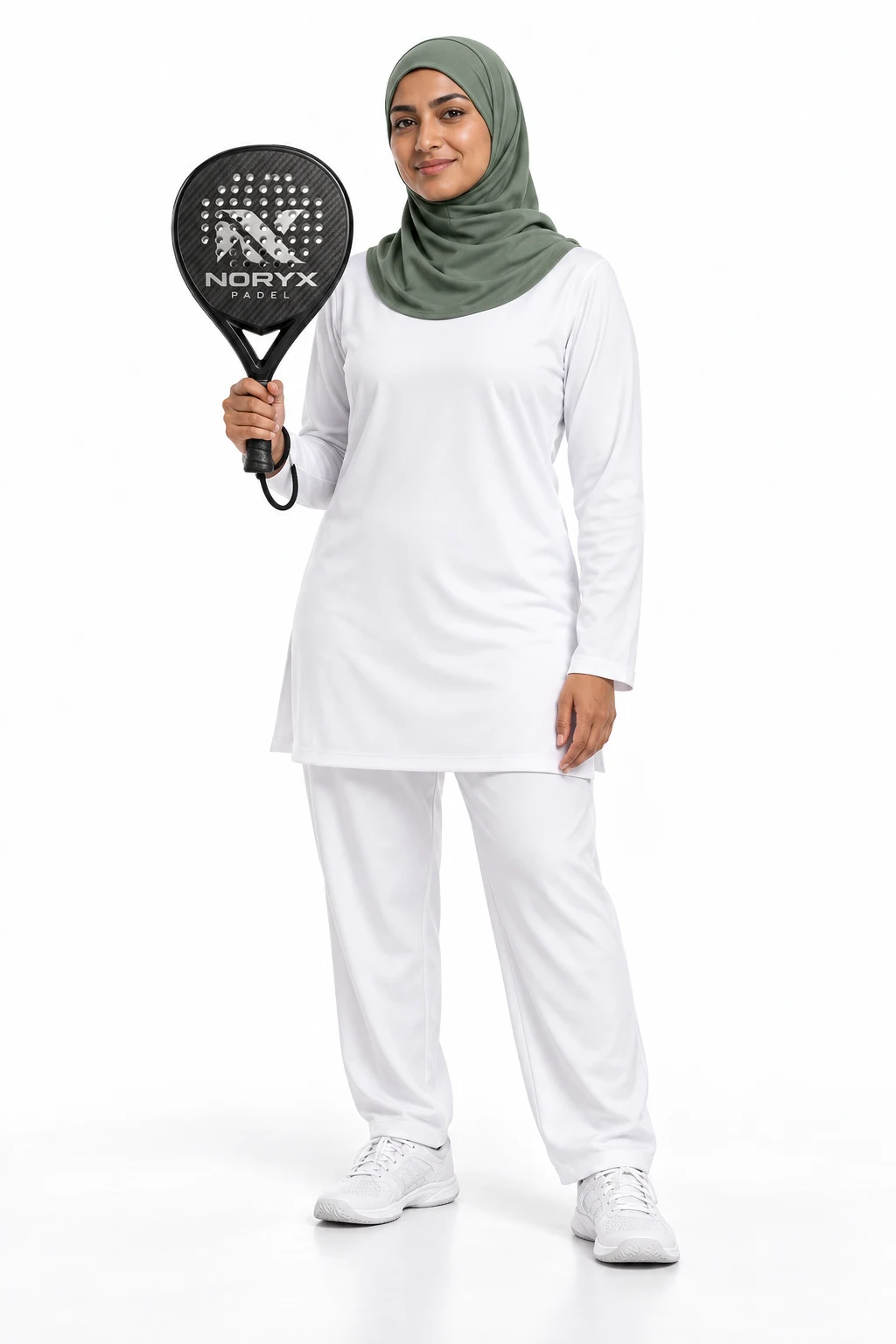 A woman wearing a sage sports hijab, a loose long sleeved white tunic and full length trousers, holding a black NORYX racket